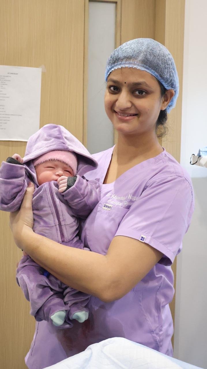 Dr. Khushboo Nagpal in clinical scrubs holding a newborn baby